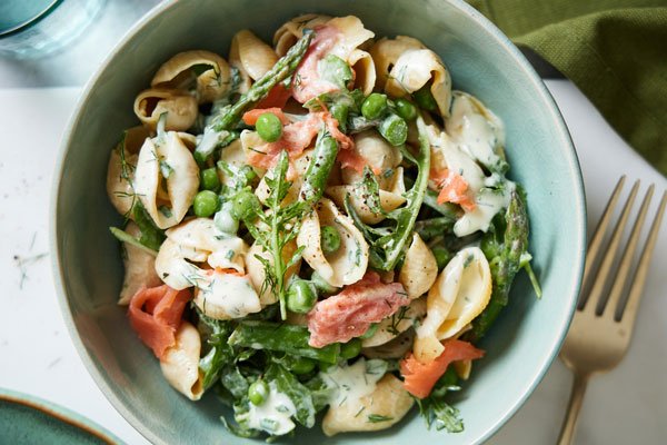Salade froide composée de saumon fumé, conchiglioni au pesto, stracciatella crémeuse, romaine et tomates cerises, servie dans une assiette colorée